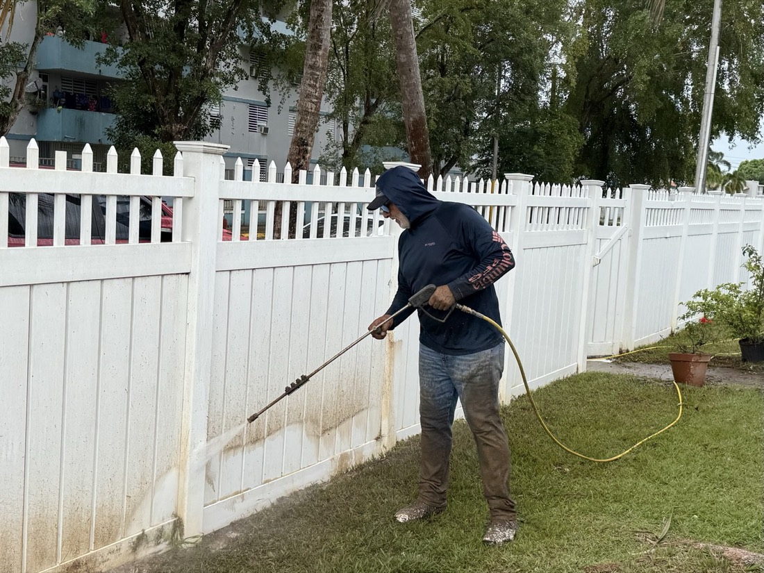 Técnico lavando a presión una verja blanca con moho en la base